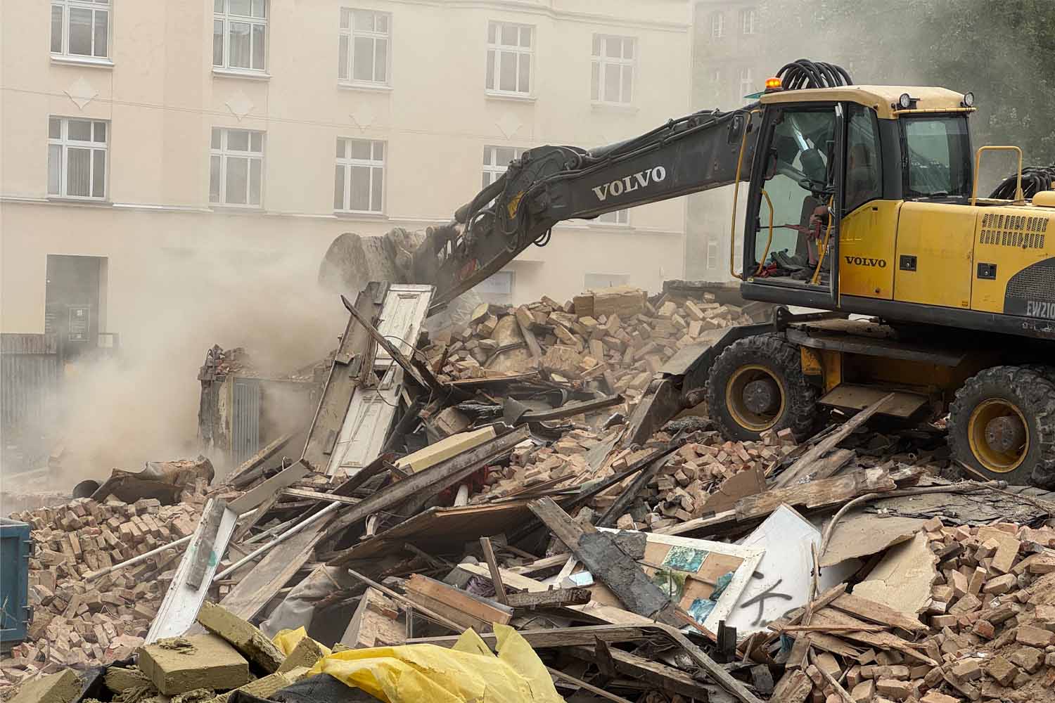Koparka podczas rozbiórki budynku wśród gruzu i pozostałych materiałów